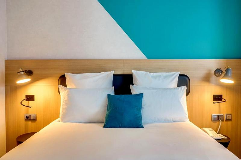 A bed with white linens and a colorful wall behind it.