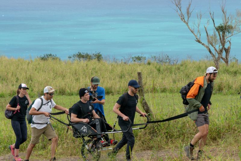 A group of friends travers uneven lands using a joëlette wheelchair