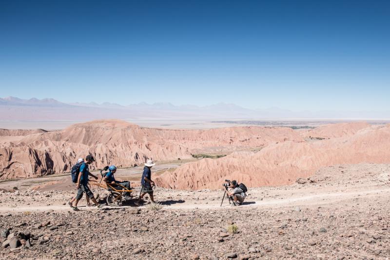 Lunar-like terrain and visitors with a Joelette chair being photographed.